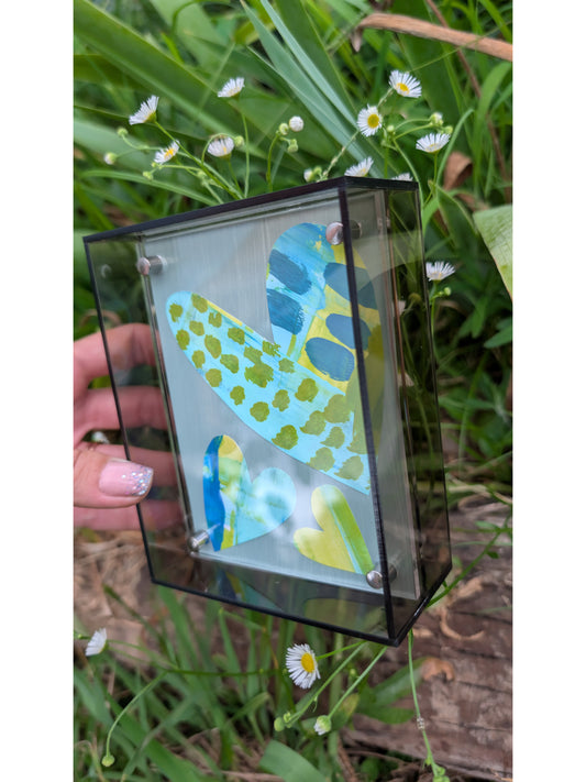 Small original heart collage with blue turquoise and green hand-painted paper hearts on gray background in gray acrylic float frame
